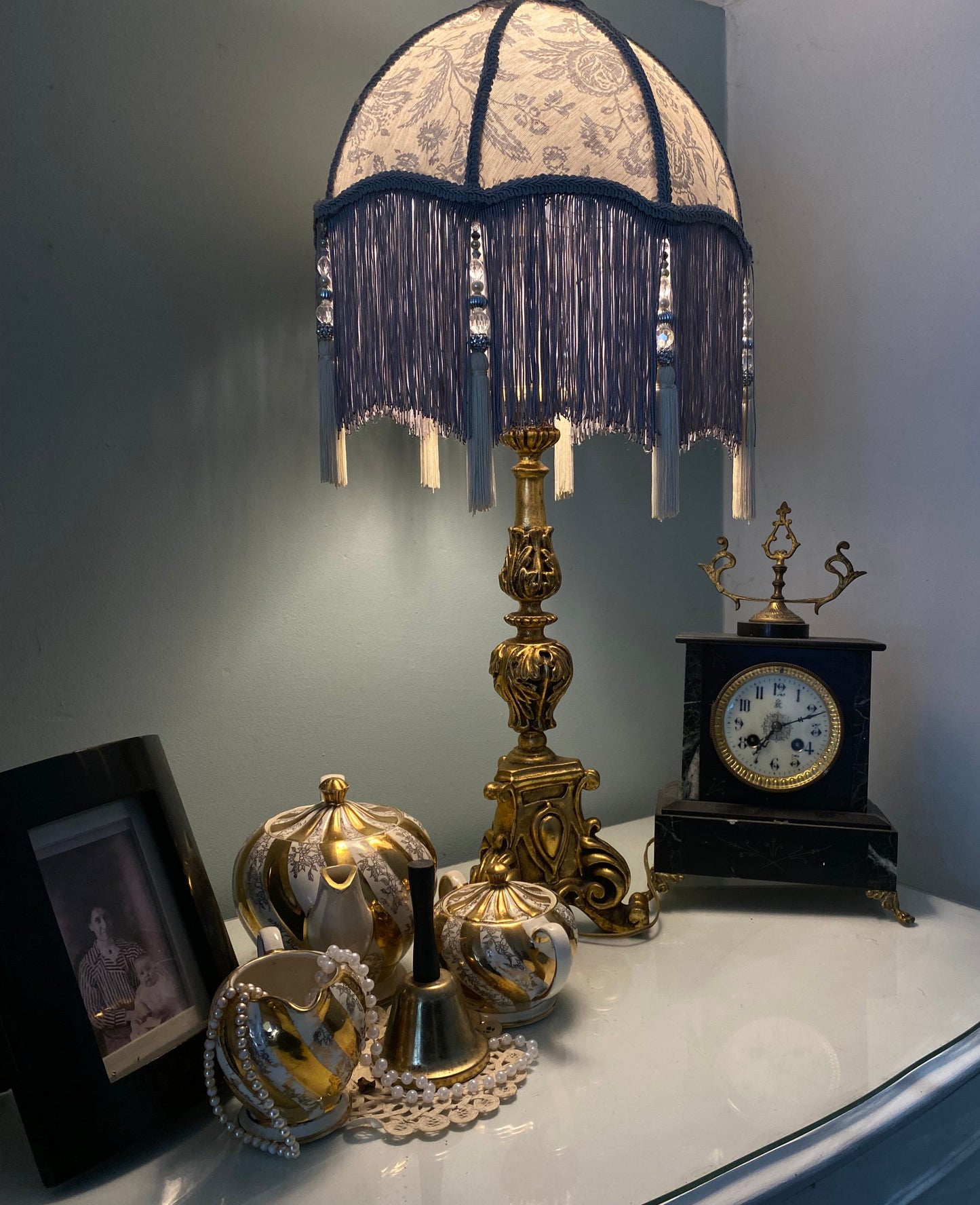Full lampshade view – A grey Victorian parachute-style lampshade in blue toile fabric, with a soft scalloped shape and a long beaded fringe lit up side angle