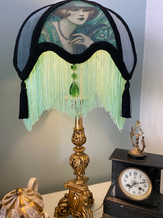 Full view – “Handmade Victorian parlour lampshade featuring an Edwardian lady image, black lace over green silk and velvet panels, with glowing green fringe and glass emerald jewels.” closer front view
