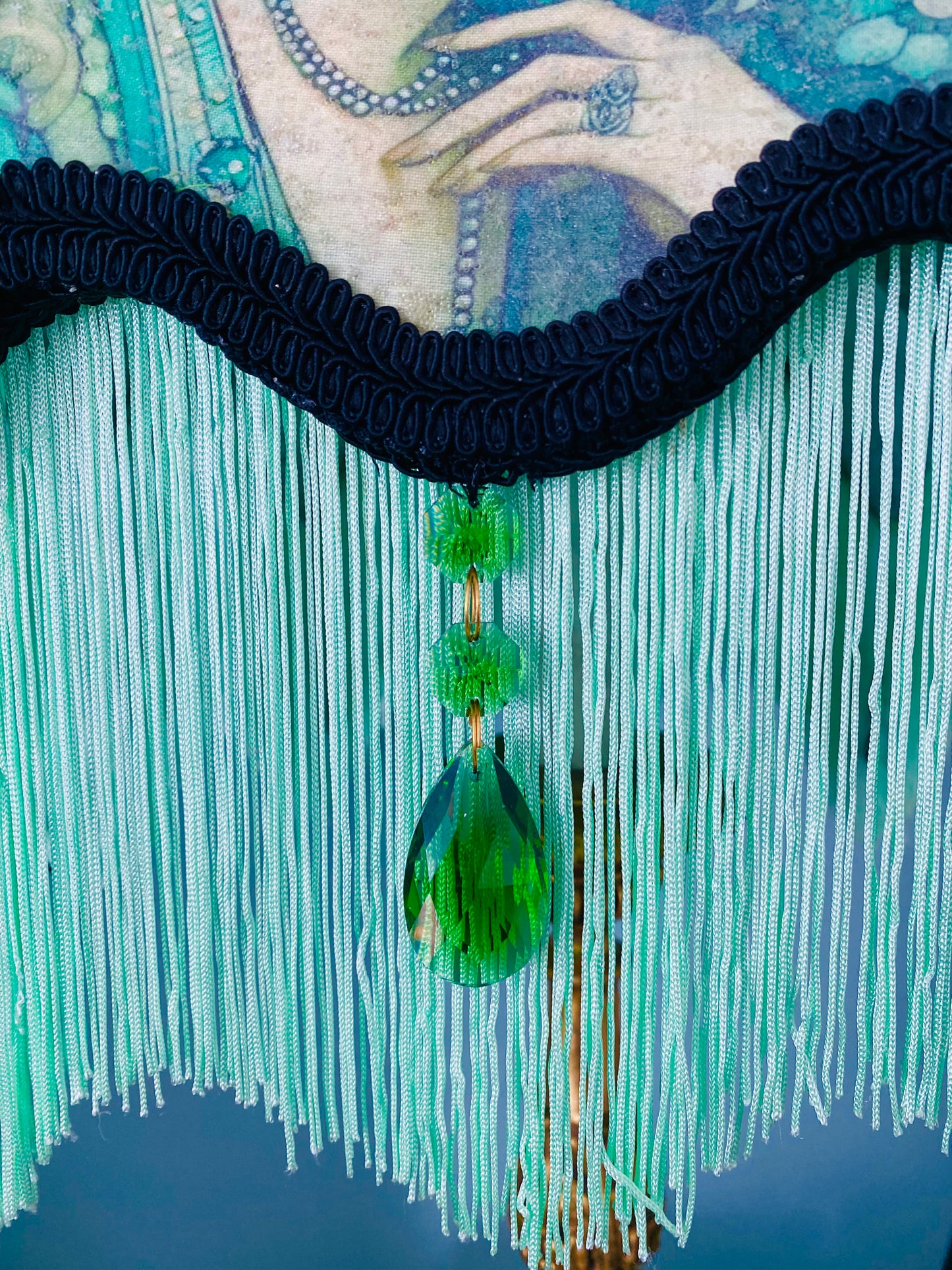 Close-up of emerald jewels – “Glass emerald jewels sparkling against green silk and black lace on an antique-inspired Victorian lampshade.”