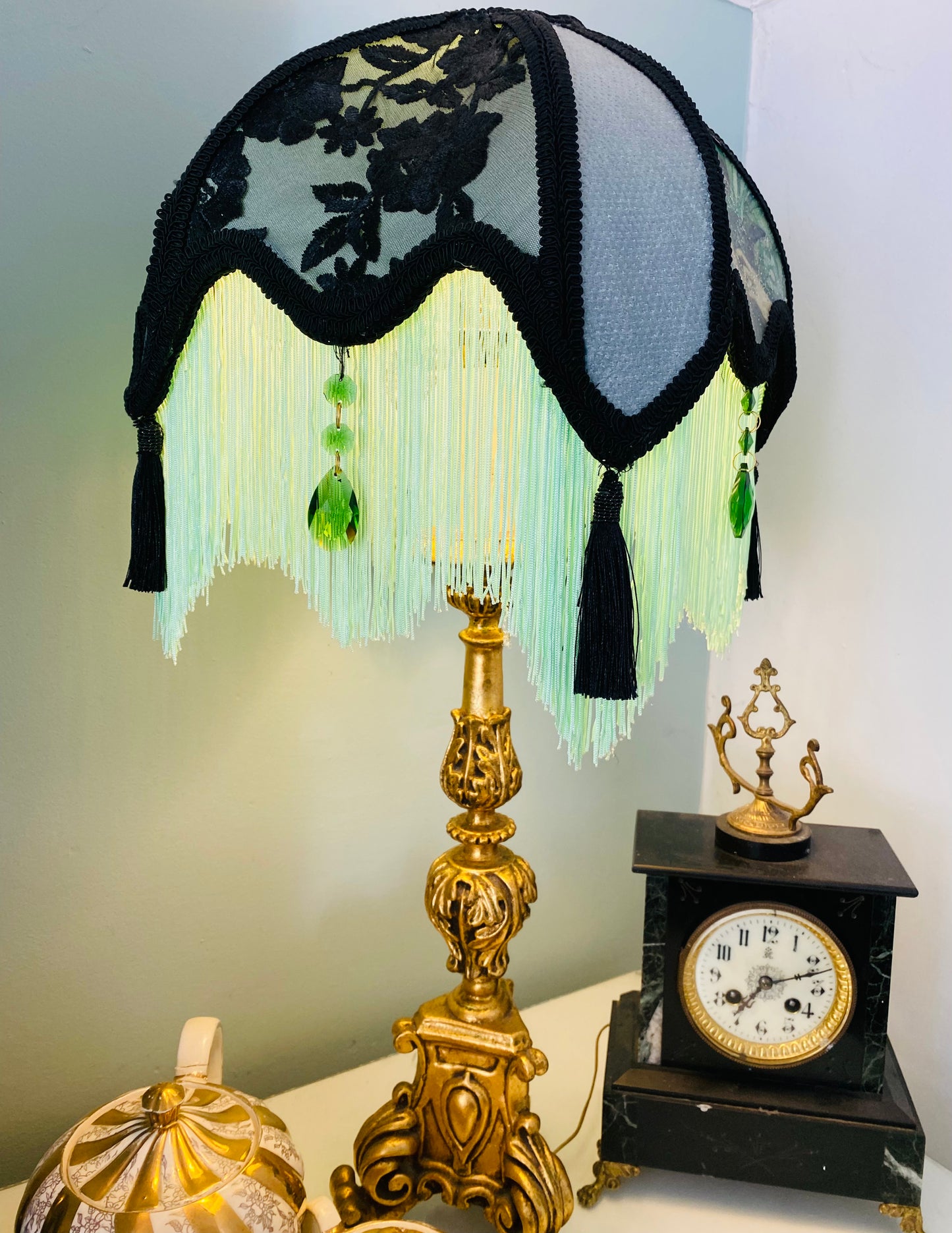 Lit lamp / ambience shot – “Victorian parlour lampshade illuminated to reveal Edwardian lady image, emerald jewels, and glowing green fringe – antique-inspired decorative lighting.”closer view