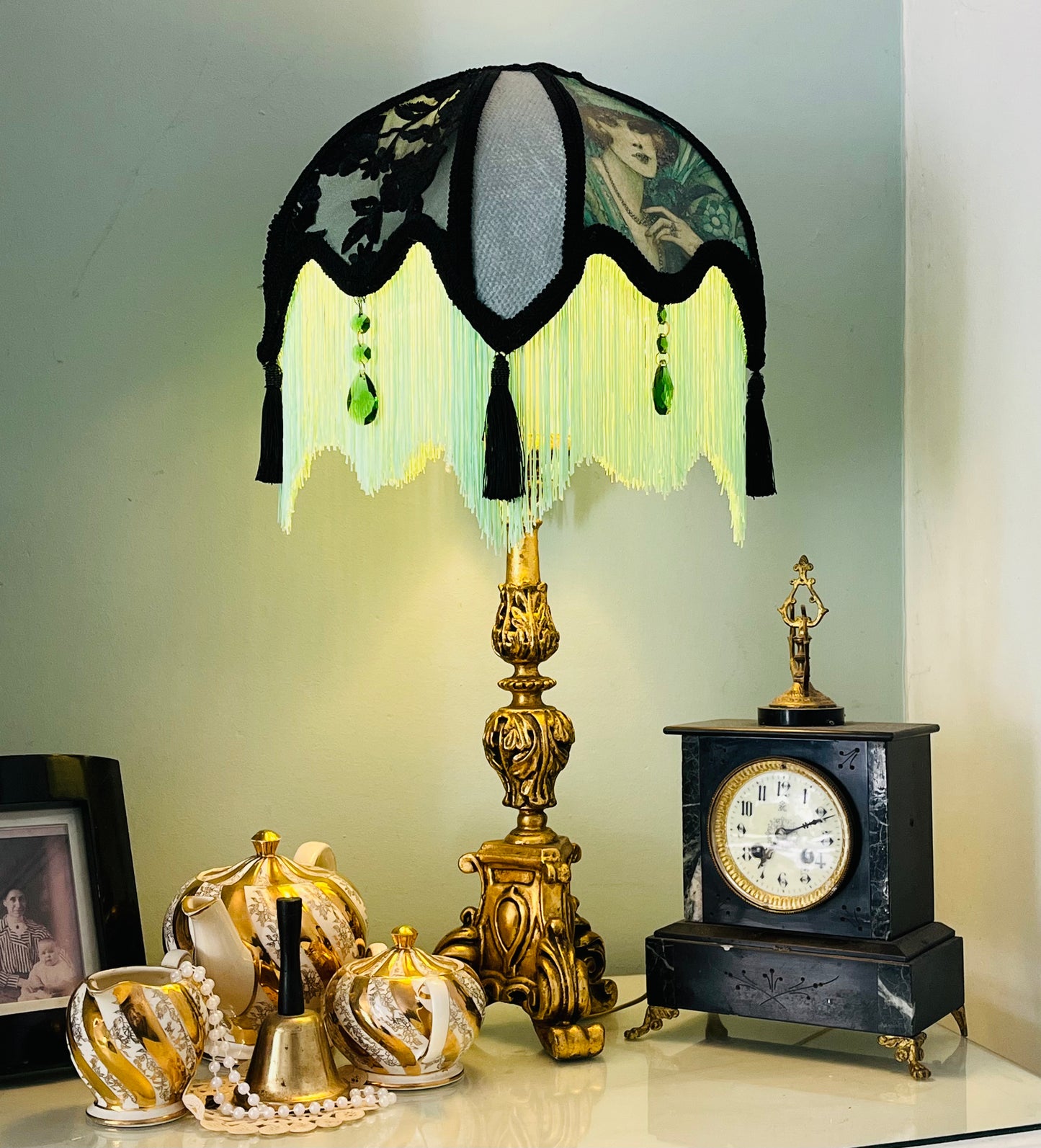 Lit lamp / ambience shot – “Victorian parlour lampshade illuminated to reveal Edwardian lady image, emerald jewels, and glowing green fringe – antique-inspired decorative lighting.”