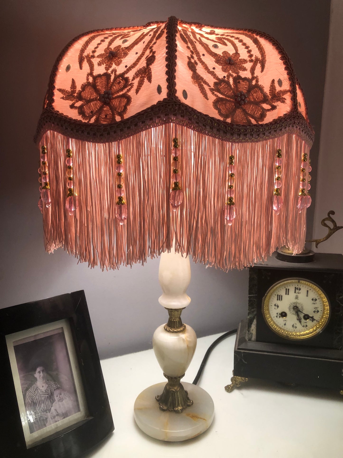 Lit full view – “Victorian pink silk floral lampshade illuminated, showing glowing floral silk, diamante sparkle, and soft pink fringe – romantic vintage lighting.”