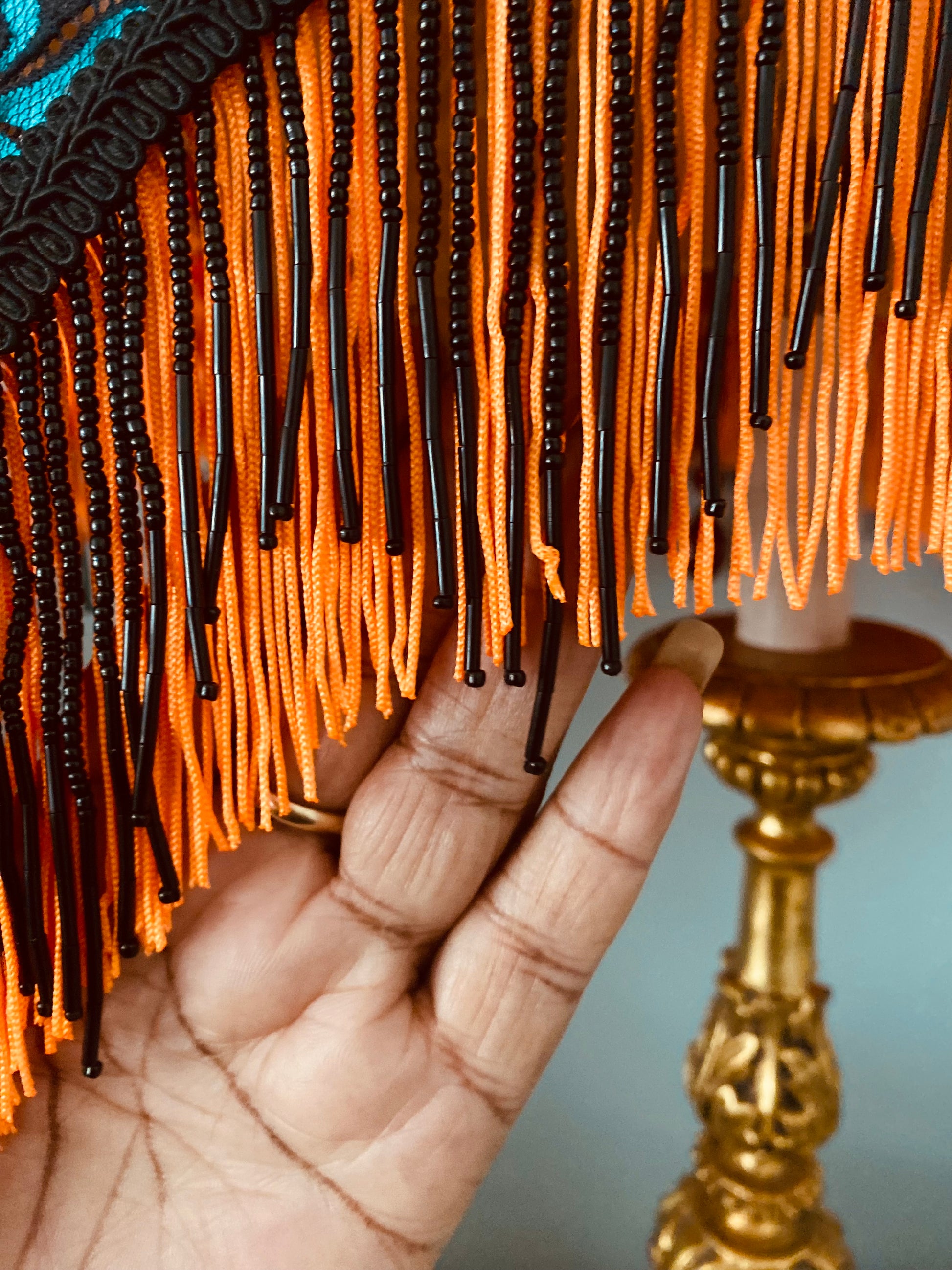 Close-up of fringe detail – “Fluorescent orange fringe with black beaded edging on a crescent Art Deco lampshade – bold handmade lighting accent evoking a sunset glow.”