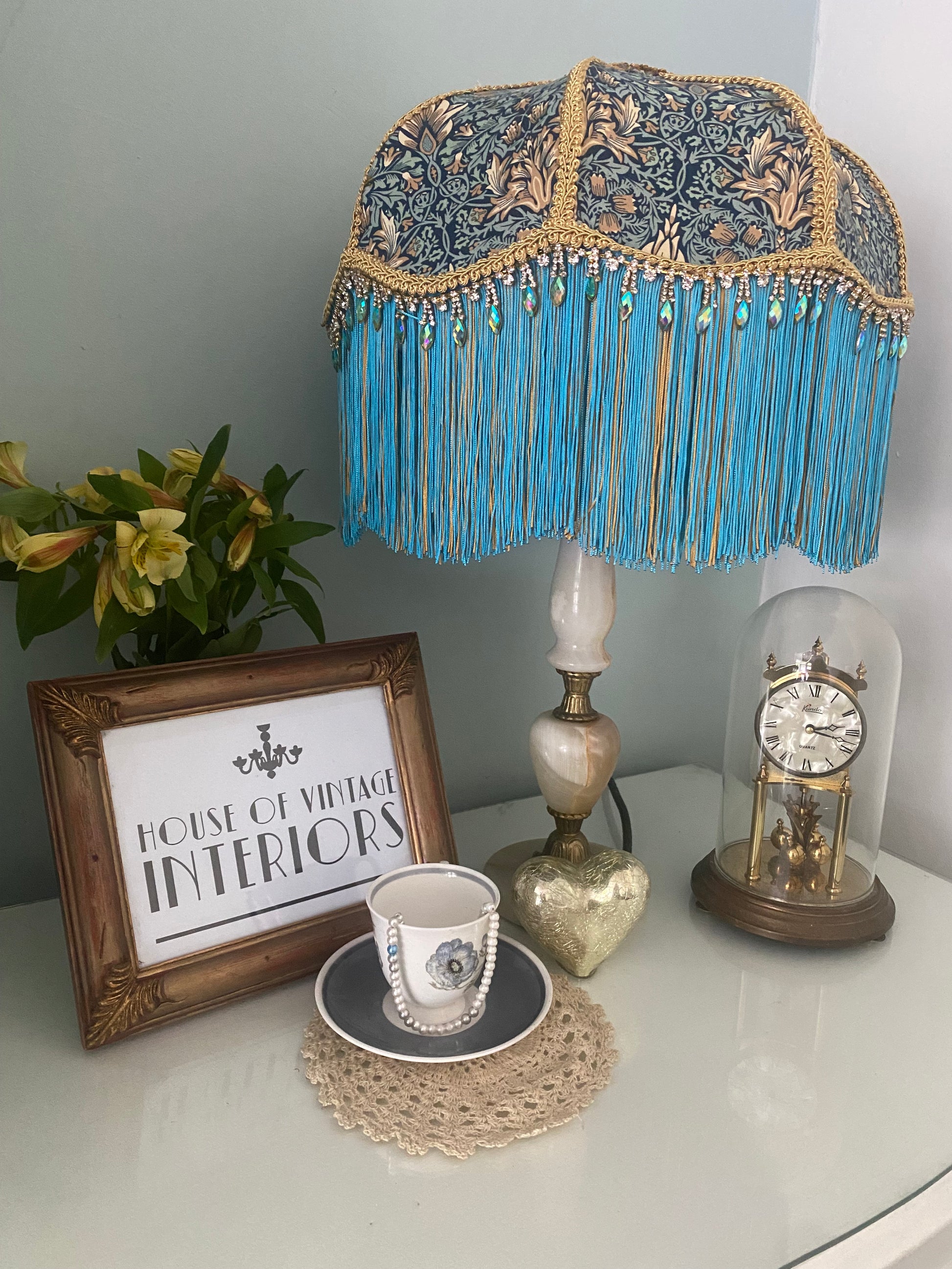 Angled shot, unlit
Handmade Art Deco lampshade in William Morris “Snakeshead” turquoise fabric, shown unlit at an angle to highlight the gold and turquoise two-tone fringe, gold braid trim, and iridescent diamanté detail — elegant Victorian-inspired fringed lighting.