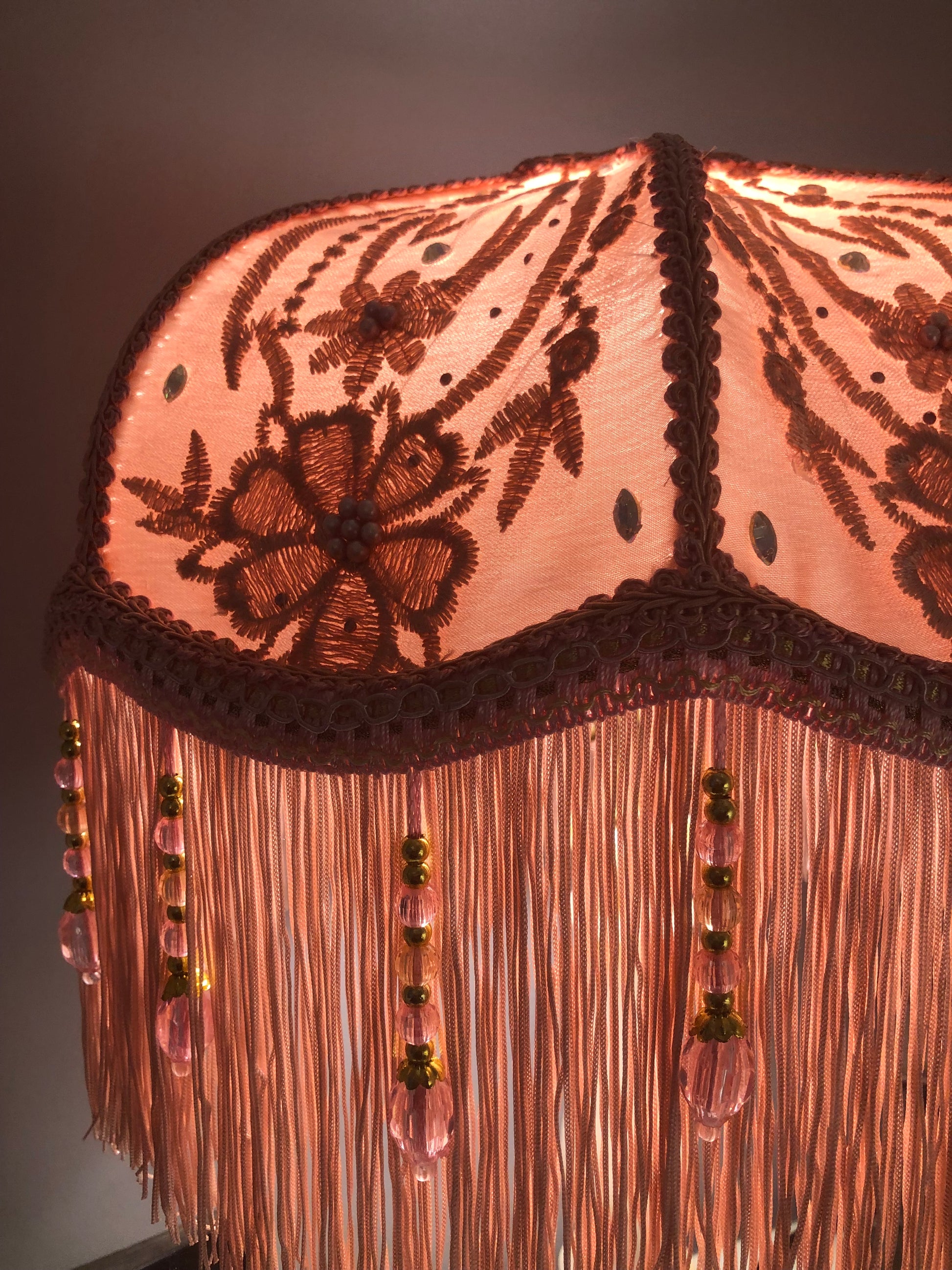 Lit close-up – “Close-up of illuminated pink Victorian lampshade with floral silk and diamante highlights, creating a warm, feminine glow.”