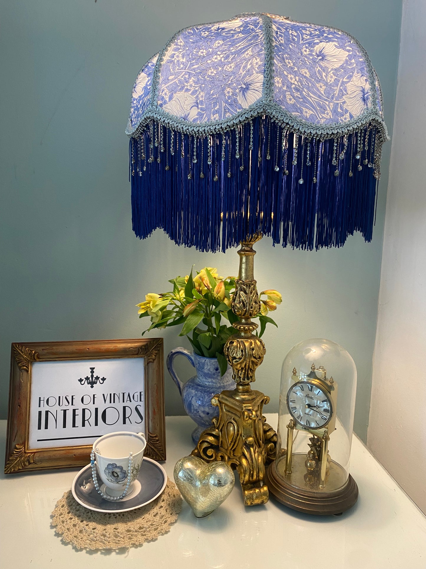 Lit ambience shot – “William Morris ‘Pimpernel’ Victorian lampshade illuminated, showing navy fringe and sparkling crystal beads in a warm vintage glow.”
