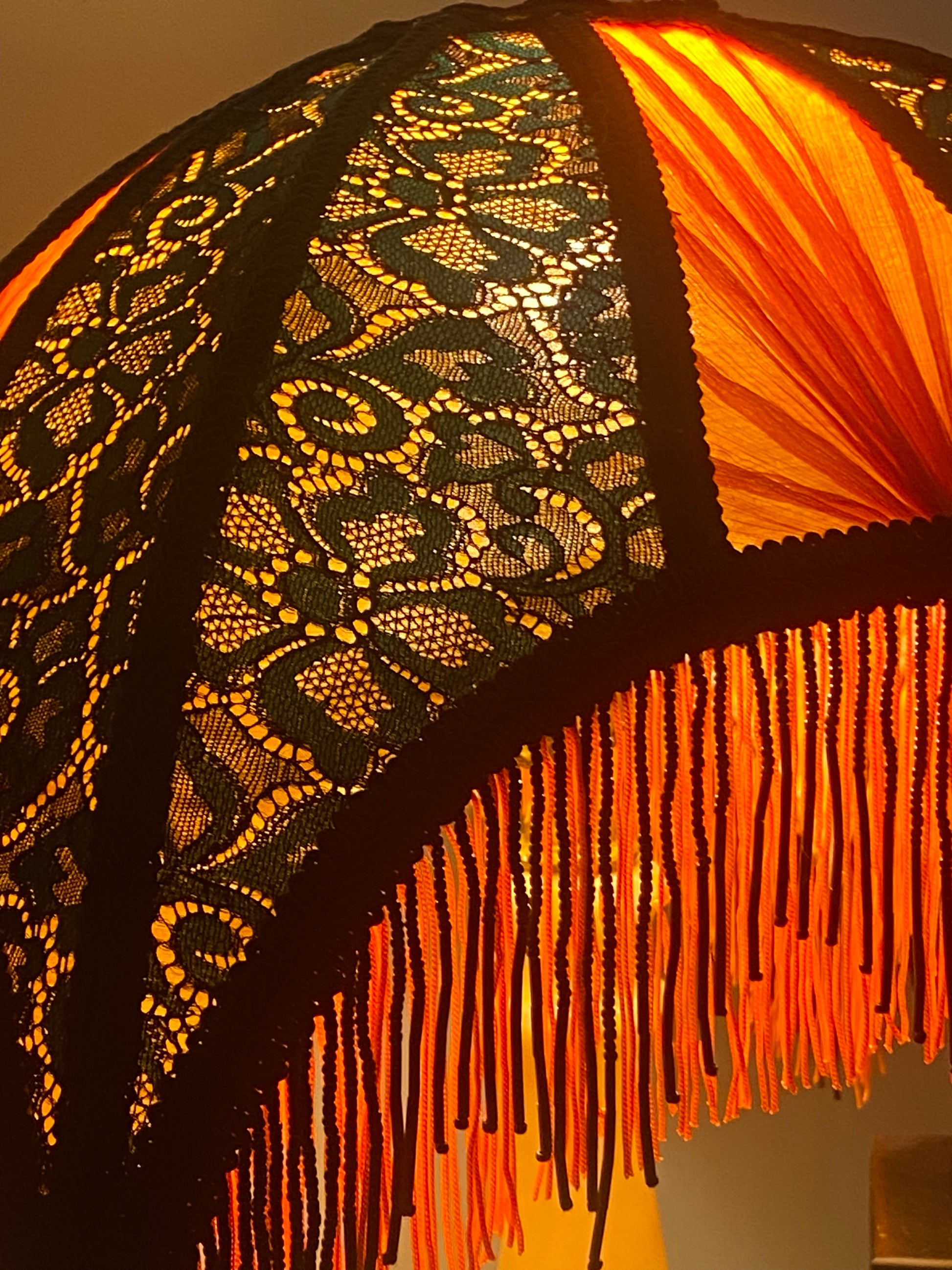 6. Angled view of the lampshade illuminated, showing the interplay of colors as the jade green lace and red chiffon glow against the orange silk base.