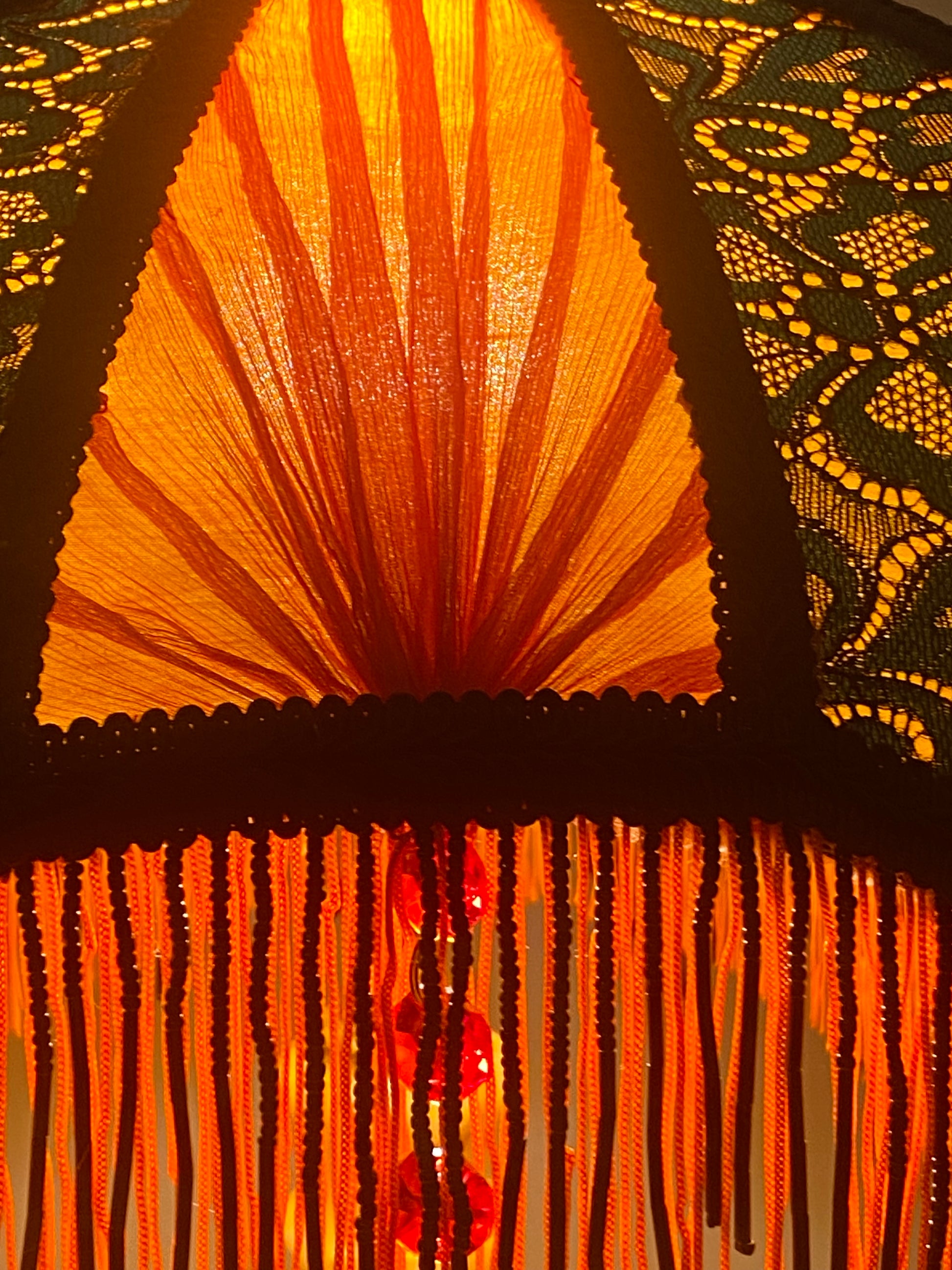 5. The Victorian lampshade lit up, glowing warmly through the orange silk and red chiffon, with lace patterns casting subtle shadows.